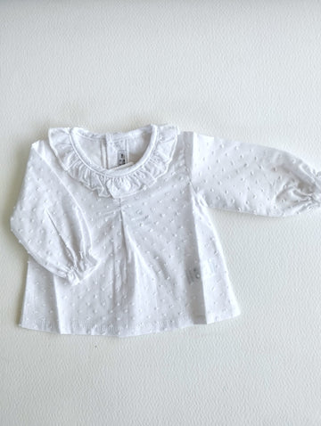 Camisa plumeti manga larda con cuello de volante y puños funcidos, en color blanco va abotonada en la espalda.
