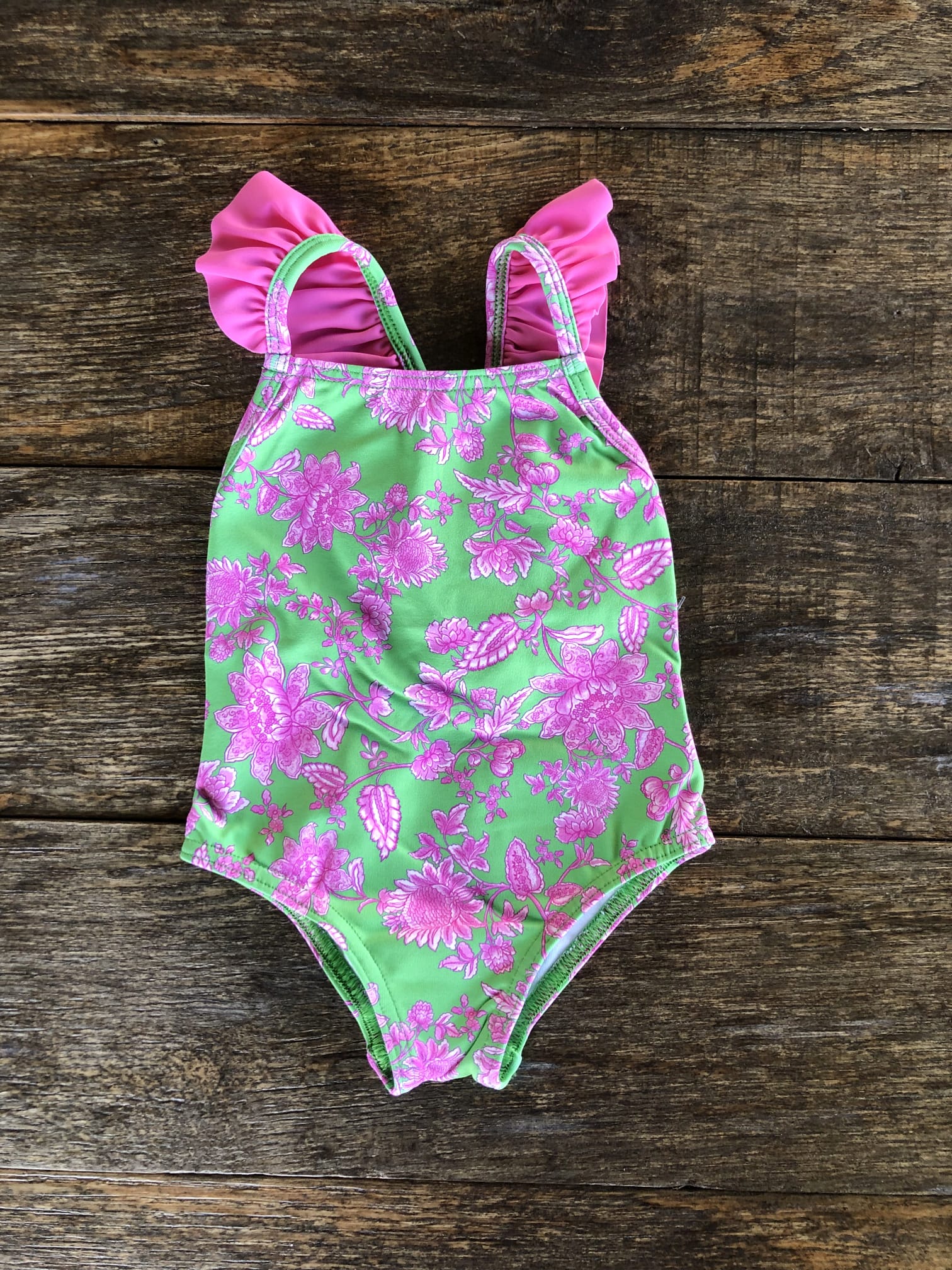 Bañador para niña verde con estampado de flores fuxia lleva volante a juego en tono fuxia en los tirantes.