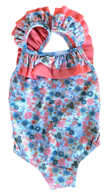 Bañador coral para niña con florecitas azules,blancas y coral sobre fondo azul clarito, lleva volante color coral en el delantero y los tirantes