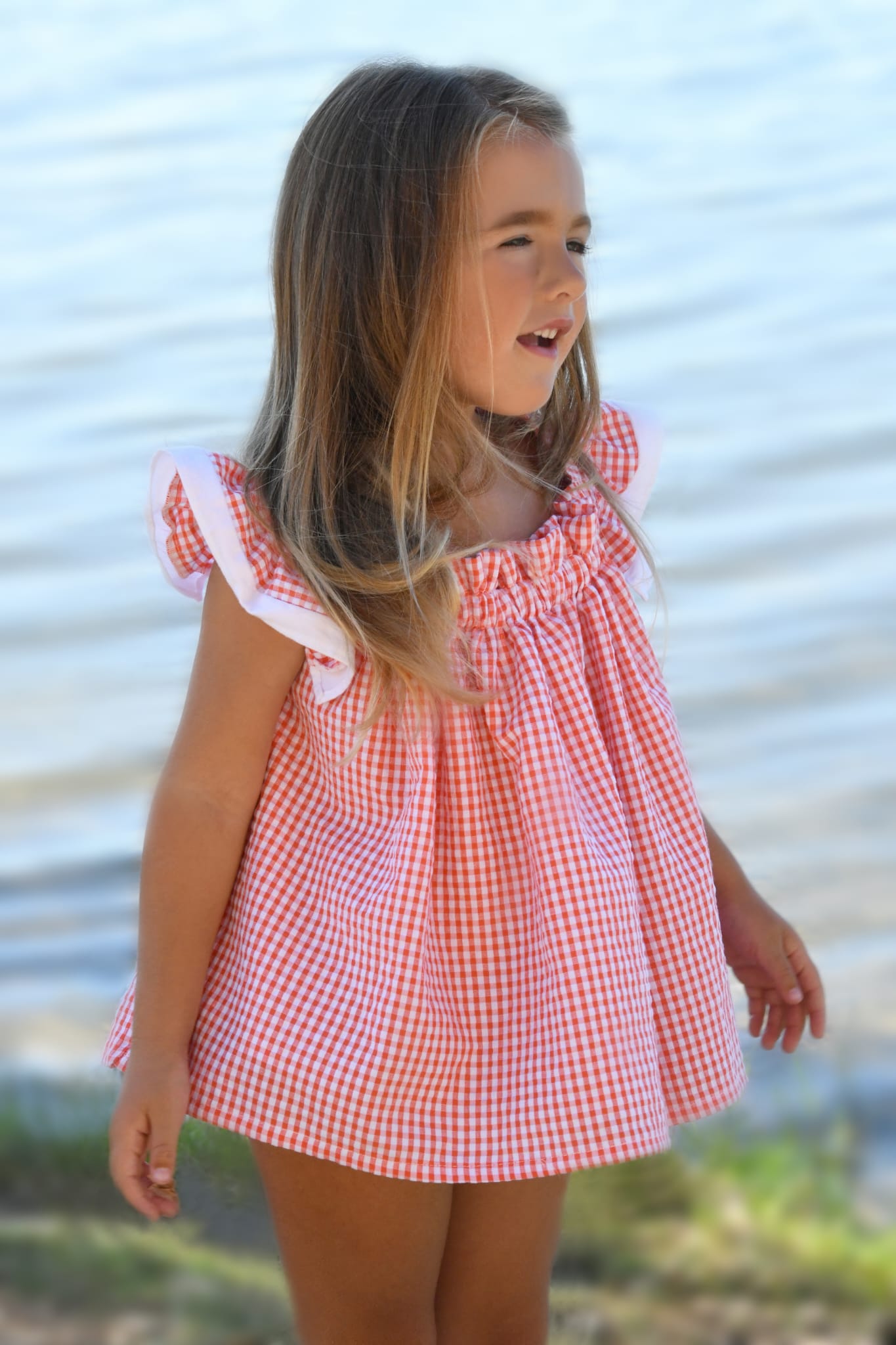 Blusa vichy Lili de Boetie kids, en color coral y blanco, sin mangas, de pierna corta, abrochada en el delantero con botones de madera y cintura elástica.
