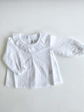 Camisa plumeti manga larda con cuello de volante y puños funcidos, en color blanco va abotonada en la espalda.
