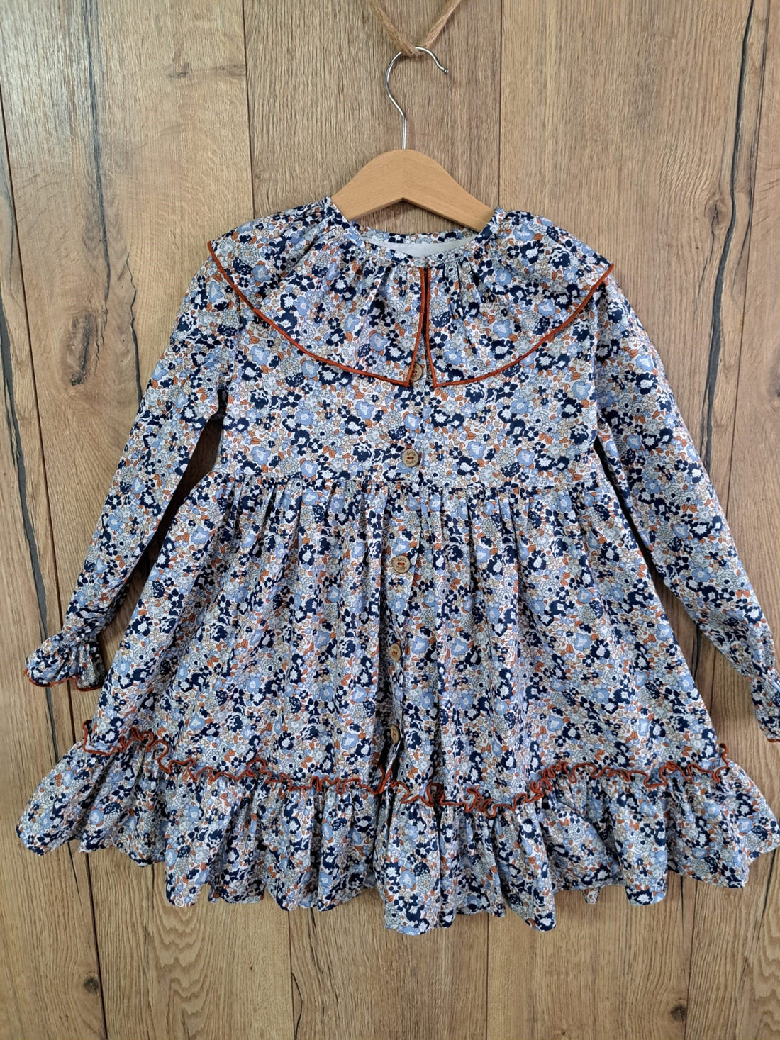 Vestido Marina de Boetiekids con flores azules y cuello con volante ribeteado en color caldera con vuelo y rematado con gran volante en la parte inferior