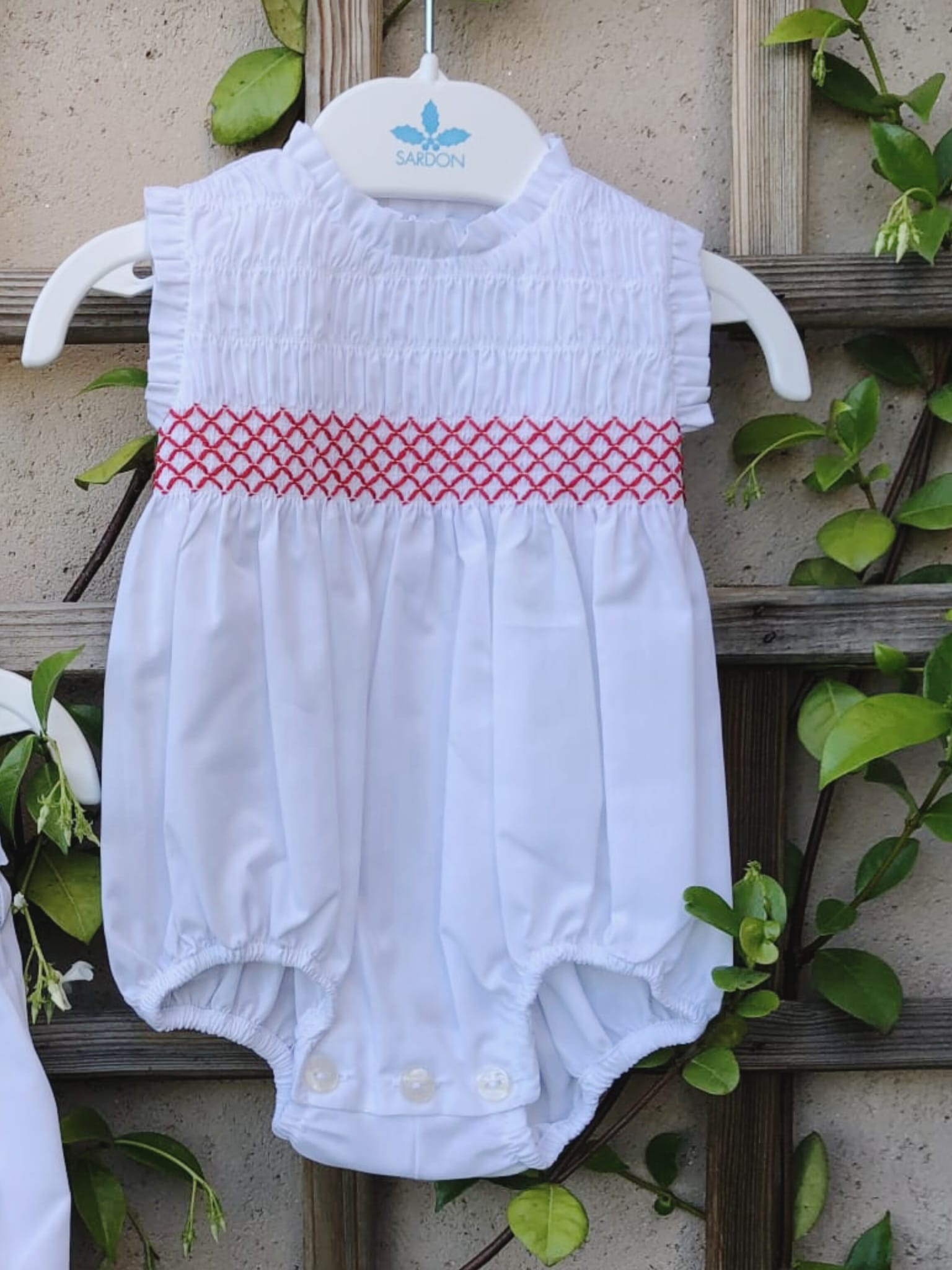 Ranita con punto de abeja en color rojo, sin mangas rematadas con volantito plisado al igual que el cuello, con delantero fruncido. Va abotonada en la espalda